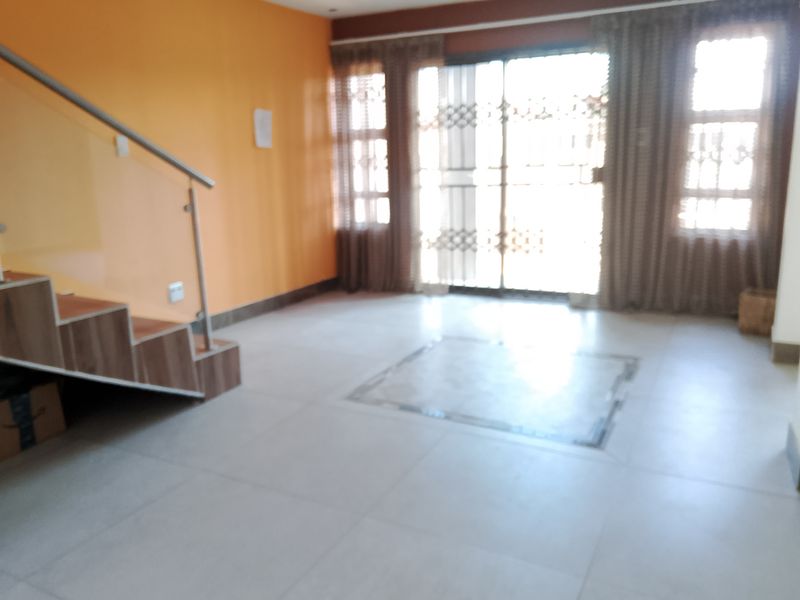An open-plan living area featuring tiled flooring, a staircase with a glass balustrade, and sliding glass doors leading to the exterior.