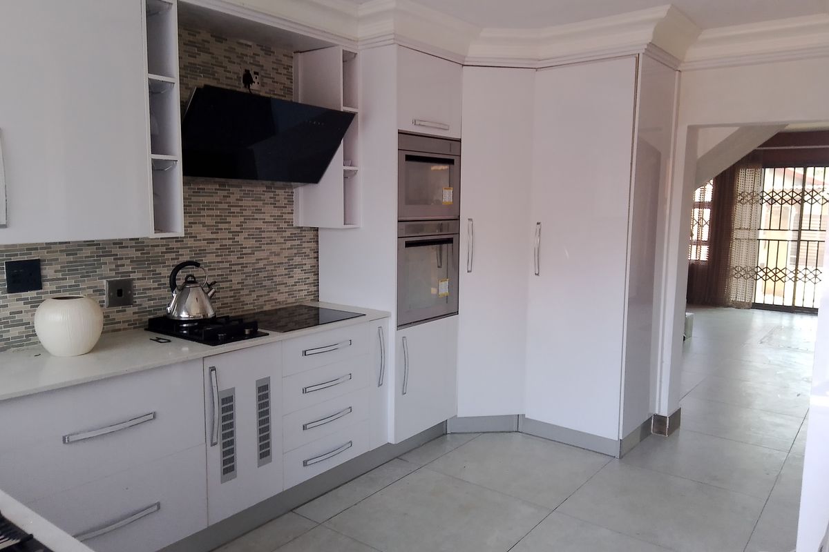Modern kitchen featuring white cabinetry, stone countertops, built-in oven and microwave, and a stylish tiled splashback with integrated extractor fan.