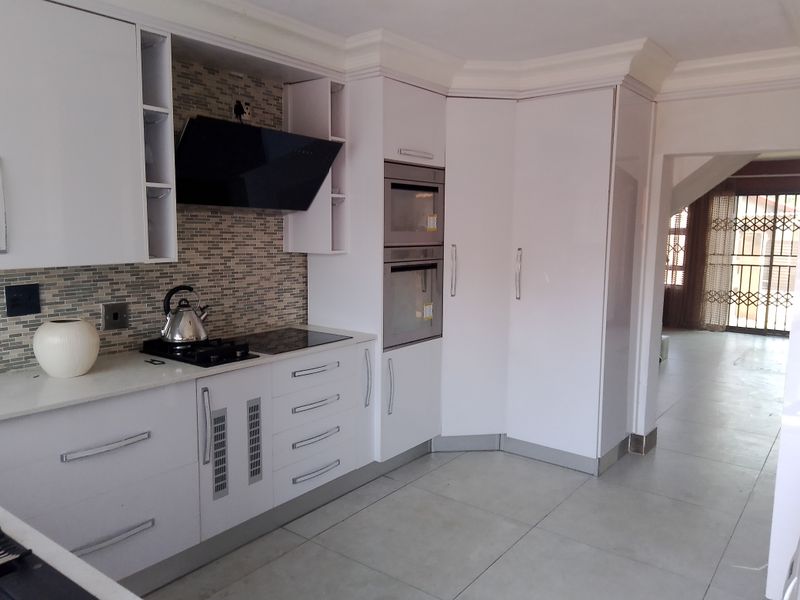 Modern kitchen featuring white cabinetry, stone countertops, built-in oven and microwave, and a stylish tiled splashback with integrated extractor fan.