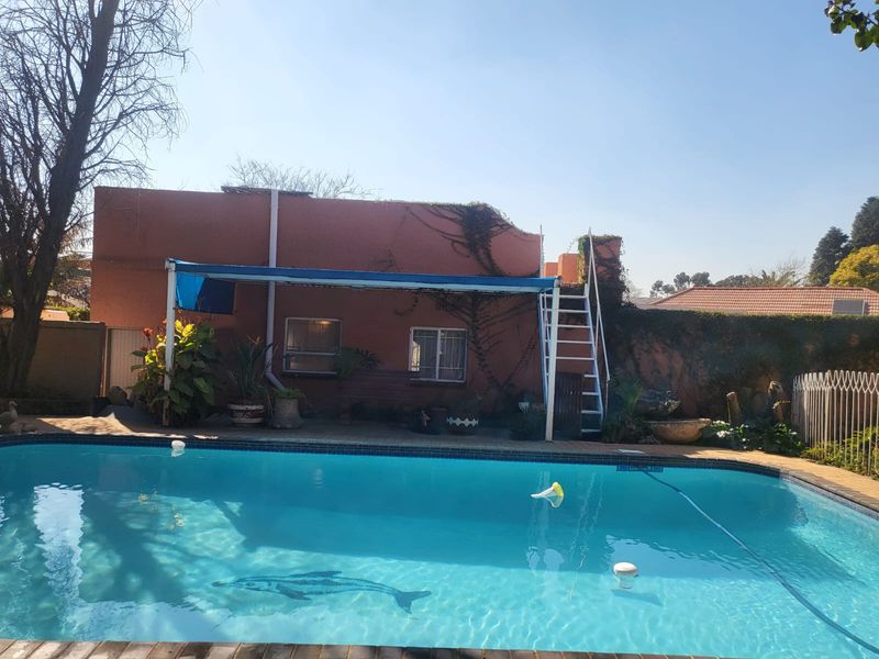 Outdoor pool area featuring a swimming pool, fixed ladder, and a covered patio section against the rear building elevation.