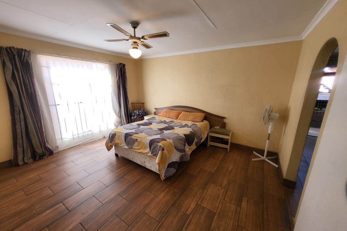 A spacious bedroom featuring tiled flooring, a ceiling fan, and an arched entryway, offering a functional layout with potential for modern updates.