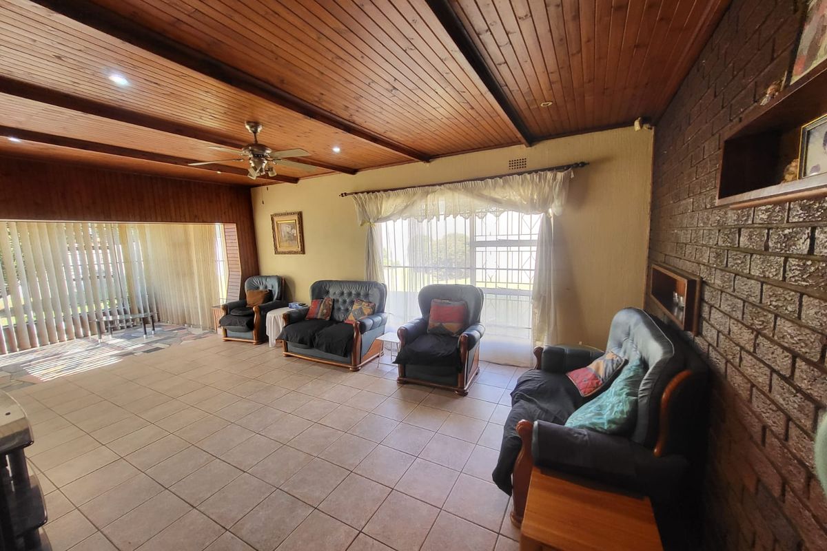 Spacious living room featuring a warm timber-clad ceiling, exposed brick feature wall, and neutral floor tiles, offering a comfortable and traditional living space.