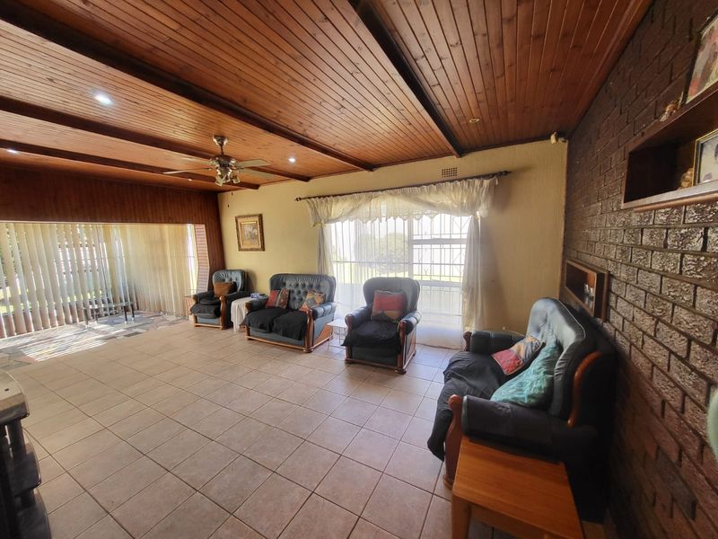 Spacious living room featuring a warm timber-clad ceiling, exposed brick feature wall, and neutral floor tiles, offering a comfortable and traditional living space.