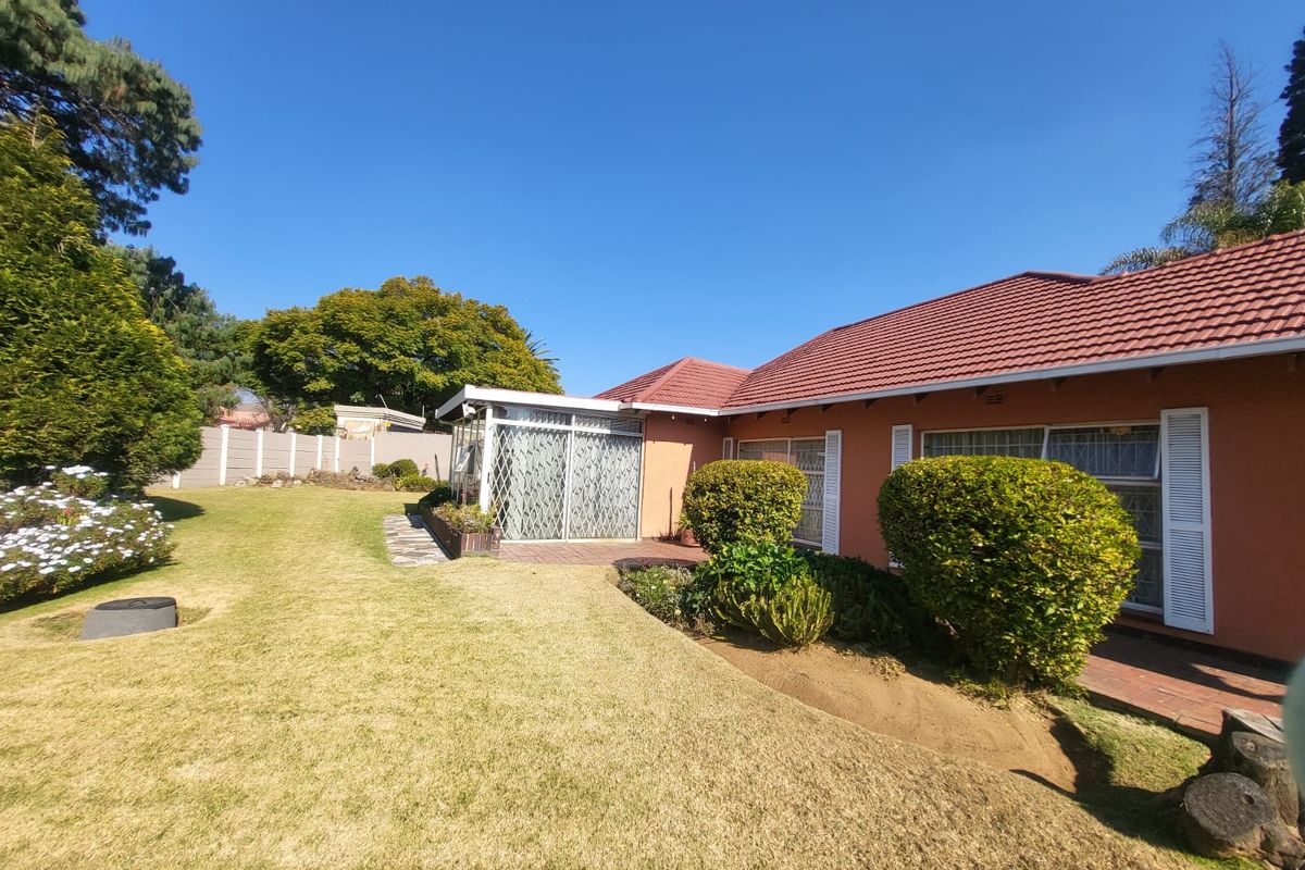Rear view of the house featuring a tiled roof, brick facade, paved patio area, and a well-maintained garden with established landscaping.