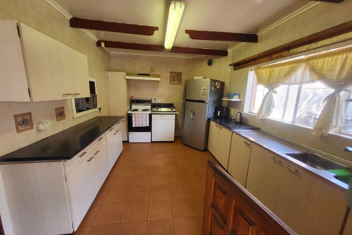 A functional kitchen featuring built-in cabinetry, laminate countertops, a stainless steel sink, and a freestanding stove, finished with tiled flooring and exposed ceiling beams.
