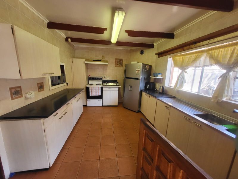 A functional kitchen featuring built-in cabinetry, laminate countertops, a stainless steel sink, and a freestanding stove, finished with tiled flooring and exposed ceiling beams.
