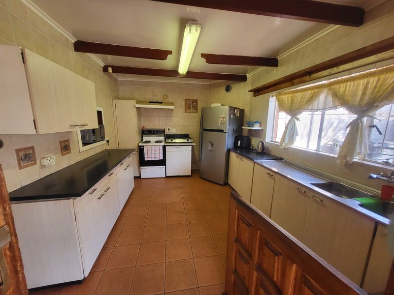 A functional kitchen featuring tiled flooring, built-in cabinetry, laminate countertops, and a freestanding stove, with exposed ceiling beams adding a rustic touch.