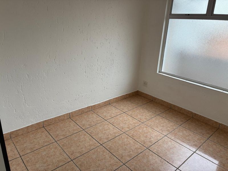A vacant bedroom featuring neutral textured walls and tiled flooring, providing a clean and versatile space ready for personalization.