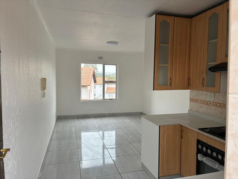 An open-plan kitchen and living area featuring neutral tiled flooring, built-in wooden cabinetry, and a functional kitchen layout with integrated appliances.