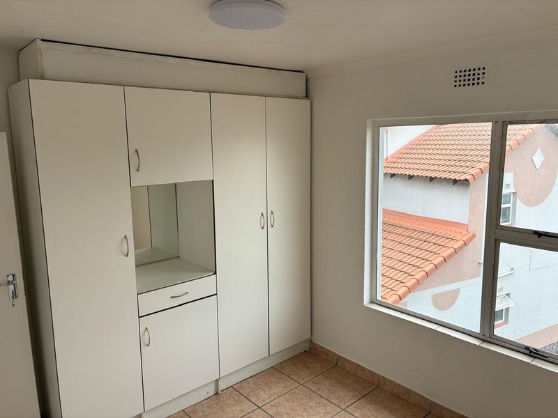 A bedroom featuring built-in cupboards with a vanity section, tiled flooring, and a window overlooking the neighbouring property.