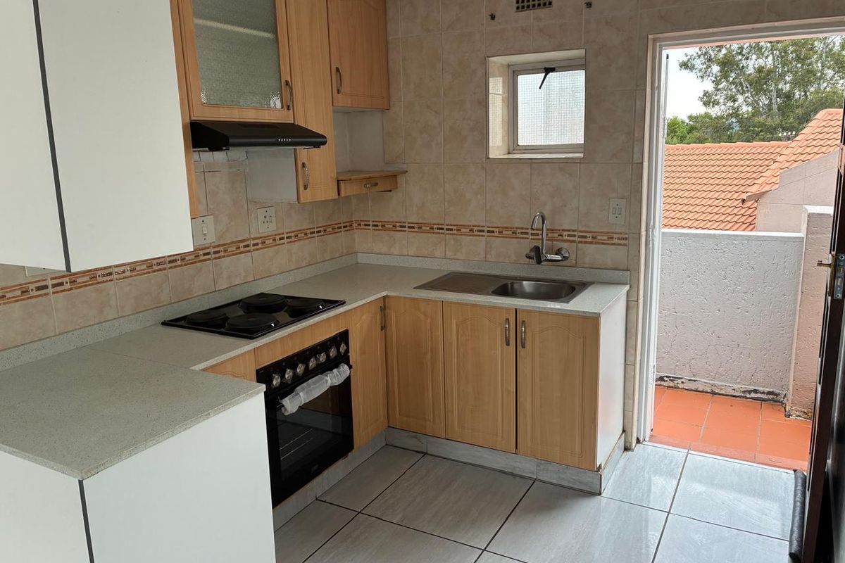 Functional kitchen featuring light wood cabinetry, built-in oven and hob, tiled backsplash, and direct access to an outdoor balcony area.