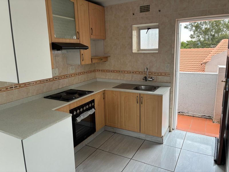 Functional kitchen featuring light wood cabinetry, built-in oven and hob, tiled backsplash, and direct access to an outdoor balcony area.