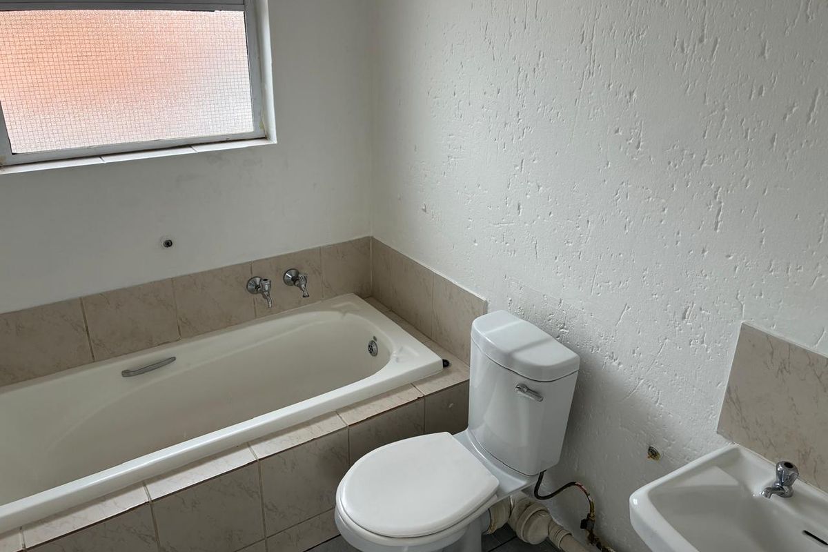 A functional bathroom featuring a built-in bathtub, toilet, and wall-mounted basin, requiring cosmetic updates and finishing touches to improve its overall condition.