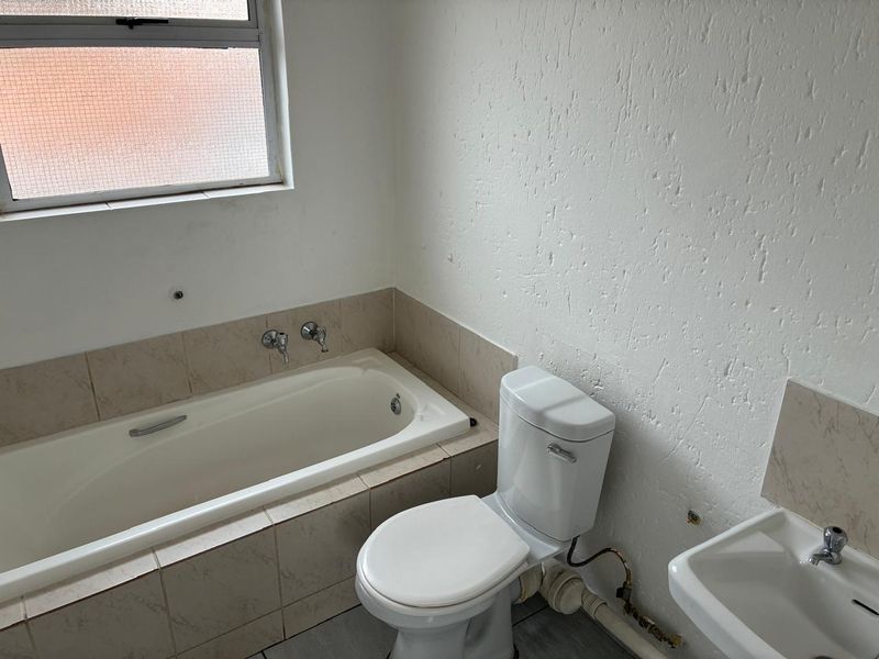 A functional bathroom featuring a built-in bathtub, toilet, and wall-mounted basin, requiring cosmetic updates and finishing touches to improve its overall condition.