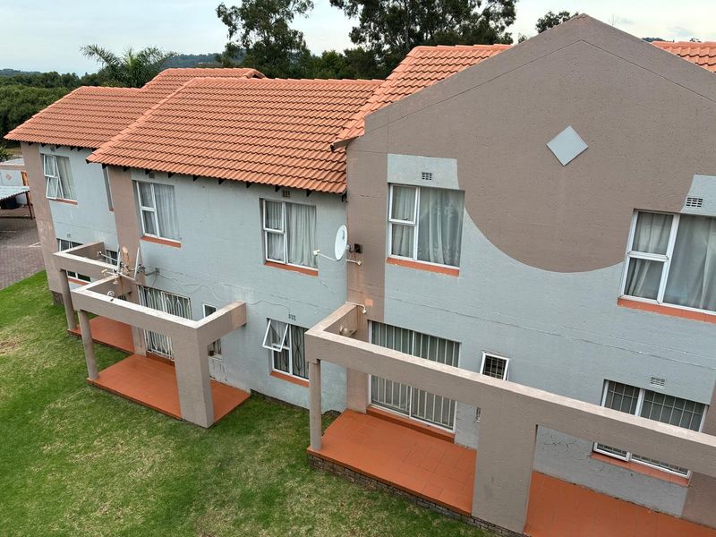 An elevated view of the rear facade of a townhouse complex, featuring tiled patios, sliding glass doors, and terracotta roof tiles.