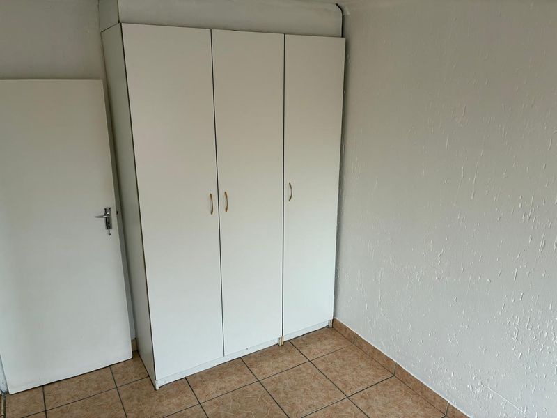 A simple bedroom featuring tiled flooring and a white built-in wardrobe with three doors.