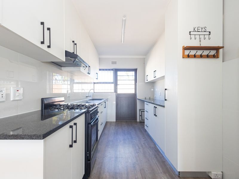 Modern galley-style kitchen featuring white cabinetry, dark granite countertops, a gas stove with extractor fan, and wood-look flooring.