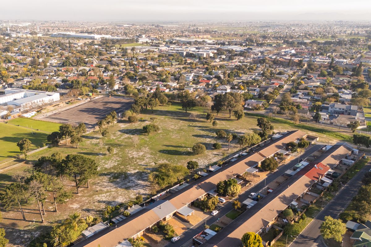 An aerial view of a residential neighborhood featuring rows of housing units, paved streets, and adjacent open parkland.