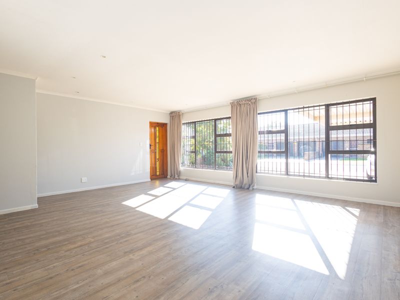 A bright and spacious living area featuring modern laminate flooring, large windows with security bars, and a timber entrance door.