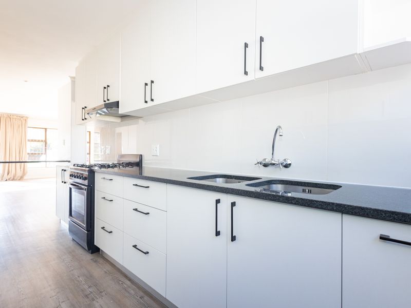 Modern kitchen featuring white cabinetry, dark granite countertops, stainless steel double sink, and a freestanding gas stove with an extractor fan.