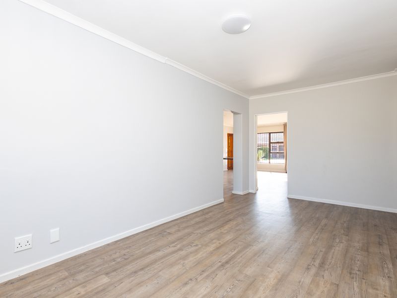 A bright, empty living room featuring modern laminate flooring, neutral walls, and coved cornicing, offering a clean and versatile space for interior design.