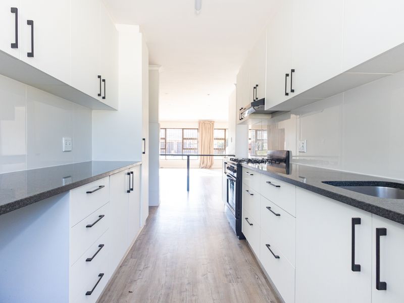 Modern galley-style kitchen featuring white cabinetry, dark stone countertops, integrated oven, extractor fan, and durable laminate flooring.