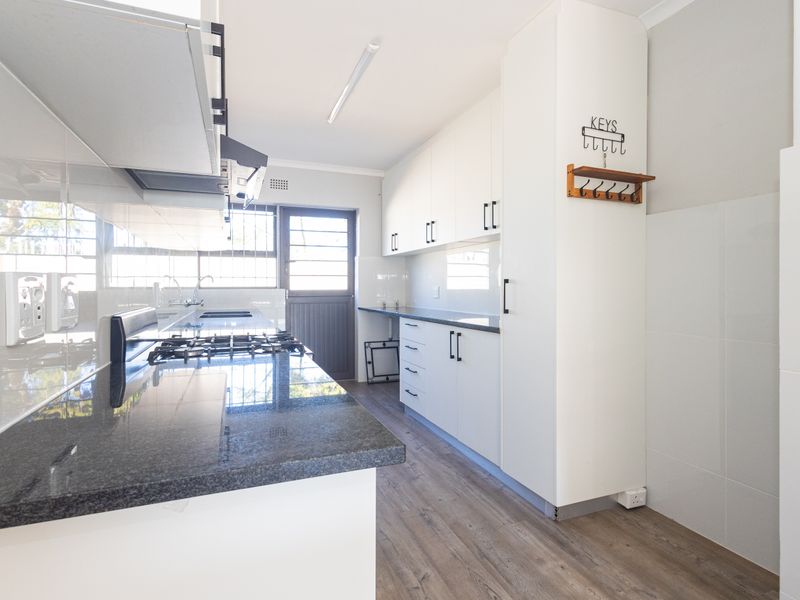 A clean, modern kitchen featuring white cabinetry, dark granite countertops, a gas hob, and durable laminate flooring with direct access to the exterior.