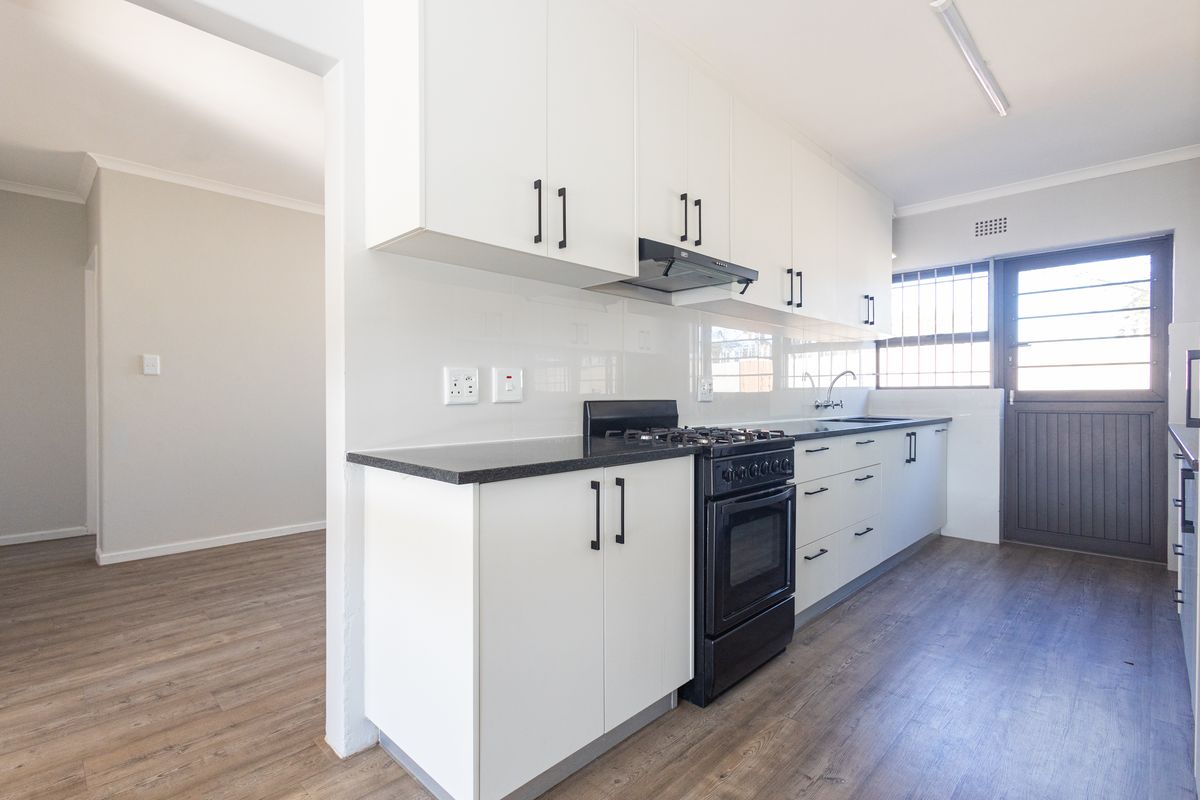 A clean, modern kitchen featuring white cabinetry, a black gas stove, laminate flooring, and direct access to the exterior.