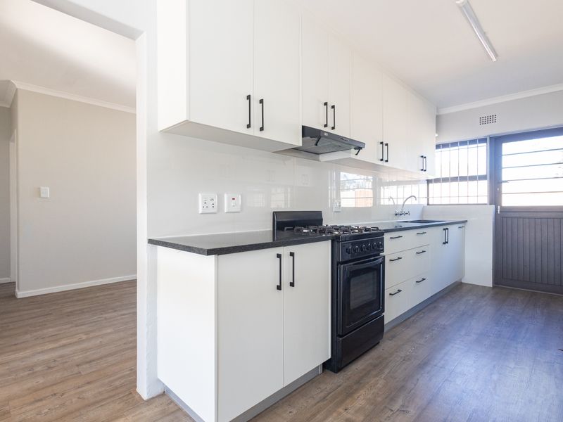 A clean, modern kitchen featuring white cabinetry, a black gas stove, laminate flooring, and direct access to the exterior.
