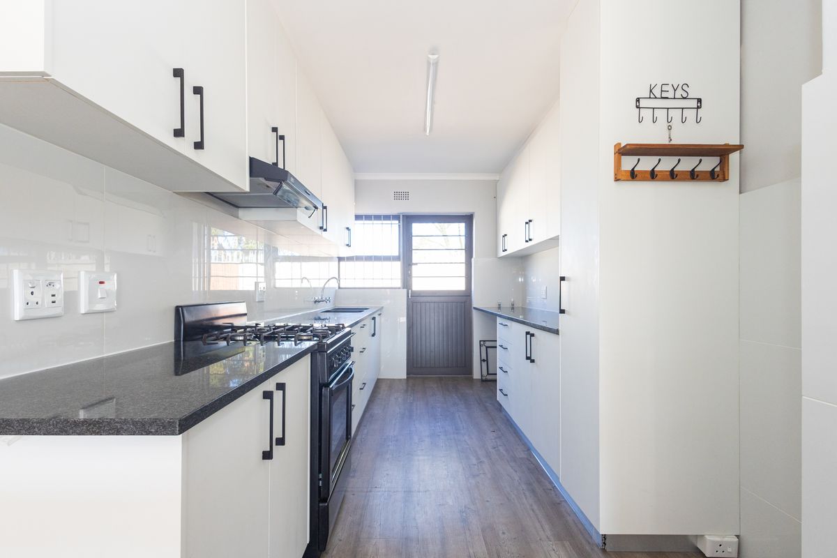 Modern galley-style kitchen featuring white cabinetry, dark granite countertops, a gas stove with extractor fan, and wood-look flooring.