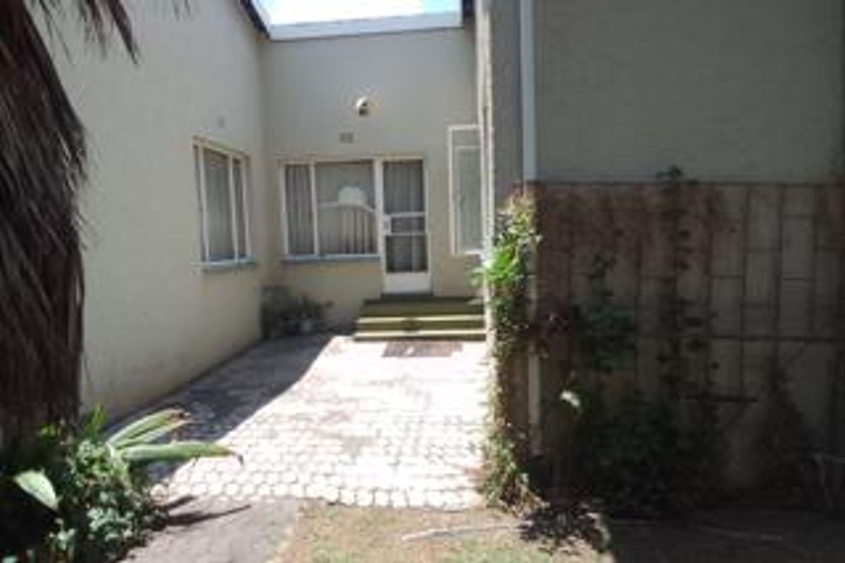 A rear exterior courtyard area featuring paved flooring, a security gate entrance, and surrounding concrete block walls with some visible weathering.