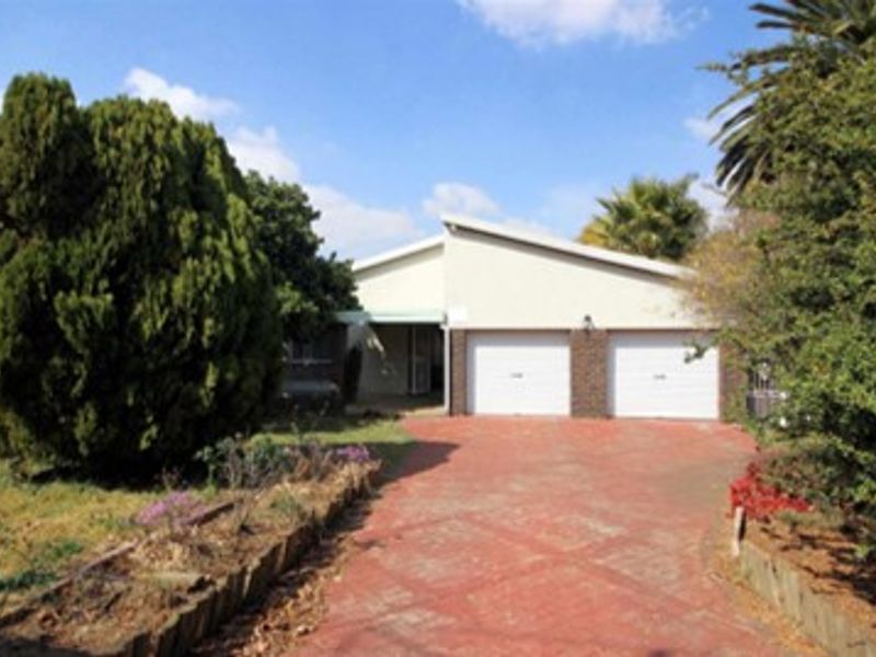 Front view of a single-story house featuring a double garage, paved driveway, and established garden landscaping.