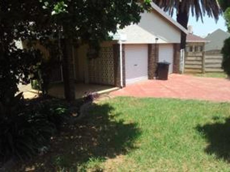 Front view of the property featuring a double garage, paved driveway, and a covered entrance area surrounded by established garden landscaping.