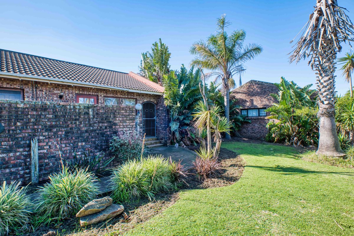 A rear exterior view of a face brick house featuring a paved walkway, established garden, and security gate access.