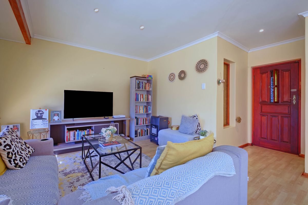 A comfortable living room featuring light-toned laminate flooring, recessed downlighting, and a solid timber front entrance door.