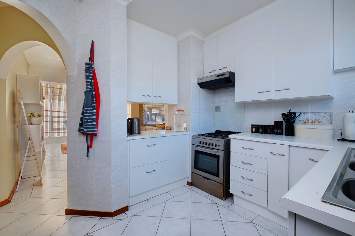 A clean, functional kitchen featuring white cabinetry, a gas stove with extractor fan, and tiled flooring, connected to an adjacent living space via an archway.