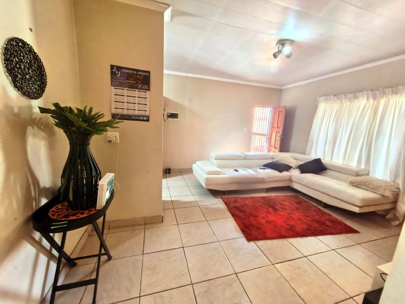 A spacious living room featuring neutral tiled flooring, coved ceilings, and direct access to an exterior security gate.