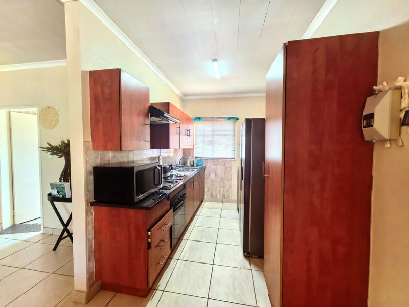 A functional galley-style kitchen featuring wood-tone cabinetry, built-in cooking appliances, tiled flooring, and a tiled backsplash, offering a practical layout for daily use.
