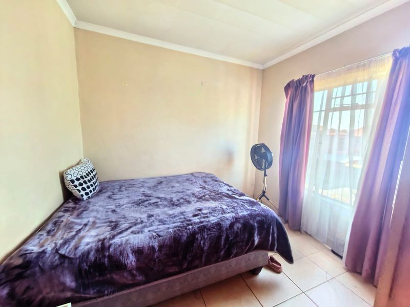 A functional bedroom featuring tiled flooring and a window with security bars, offering a neutral space ready for personalization.