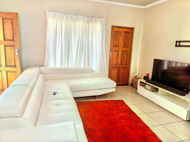 A living room featuring tiled flooring, wooden doors, and coved ceilings, providing a functional space with potential for cosmetic updates.
