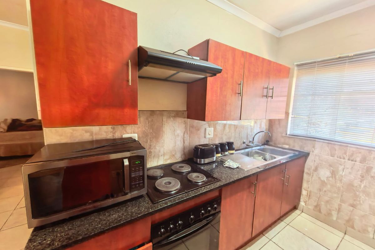 A functional kitchen featuring wood-finish cabinetry, granite countertops, a built-in oven with hob, extractor fan, and tiled backsplash with neutral floor tiles.