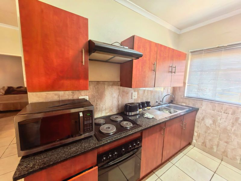 A functional kitchen featuring wood-finish cabinetry, granite countertops, a built-in oven with hob, extractor fan, and tiled backsplash with neutral floor tiles.