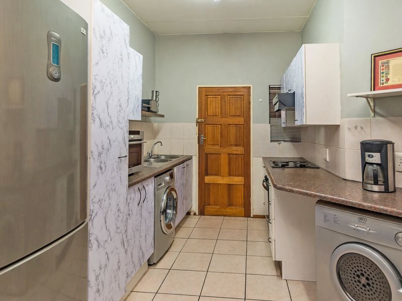 A functional kitchen featuring laminate countertops, tiled flooring, built-in cabinetry, and a tiled backsplash, providing a practical workspace for daily cooking and laundry needs.