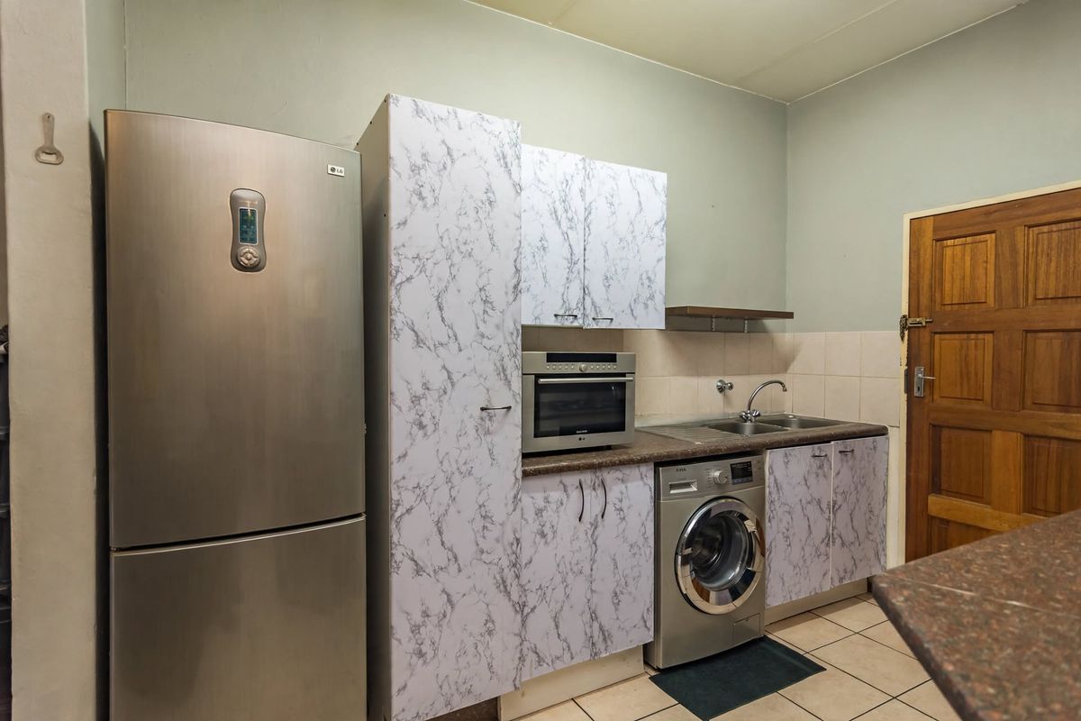 A functional kitchen area featuring built-in cabinetry, a stainless steel sink, and integrated oven space with tiled flooring and backsplash.