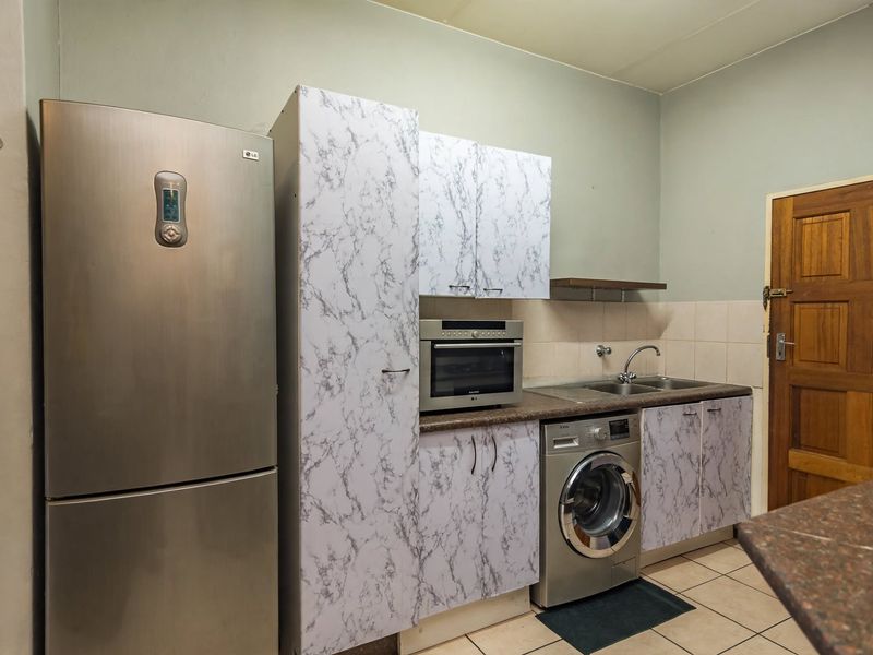 A functional kitchen area featuring built-in cabinetry, a stainless steel sink, and integrated oven space with tiled flooring and backsplash.
