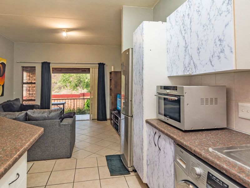 Open-plan living area featuring a functional kitchen with built-in cabinetry and tiled flooring, leading directly to a balcony through sliding glass doors.