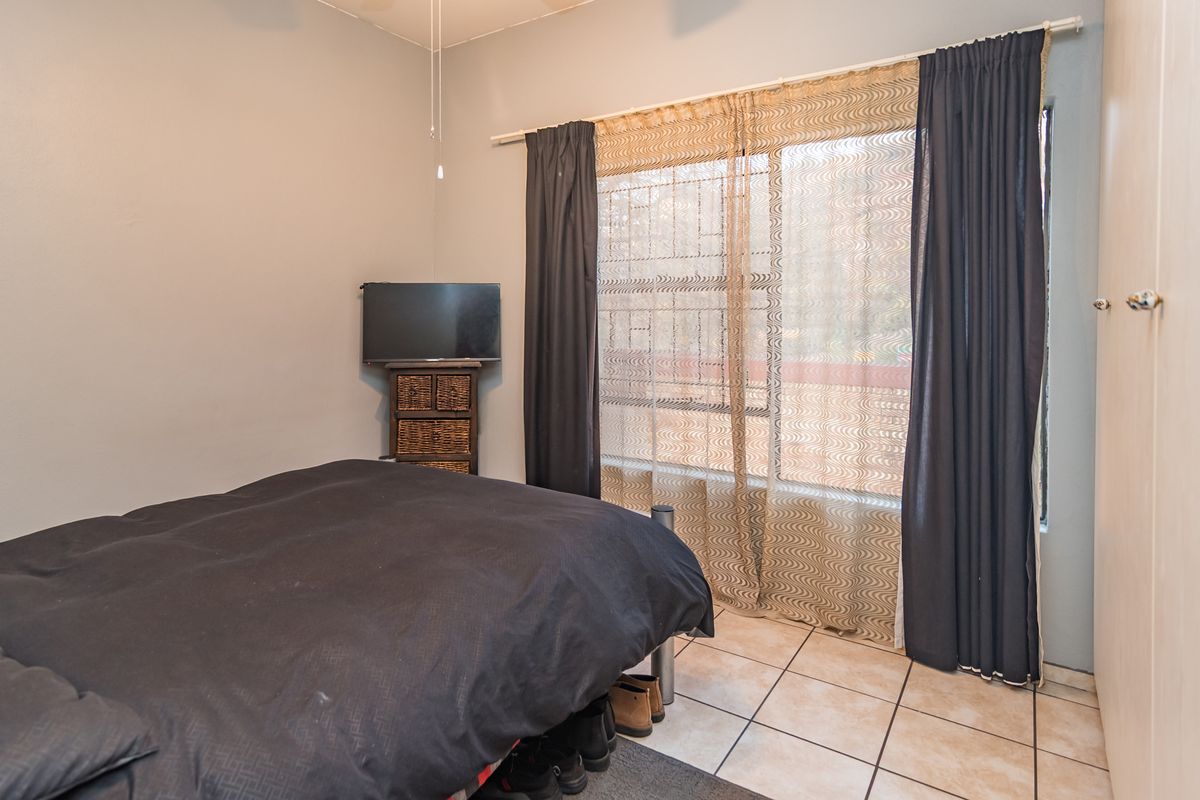 A bedroom featuring tiled flooring, a built-in cupboard, and large windows with curtain rods, providing a functional and well-lit living space.