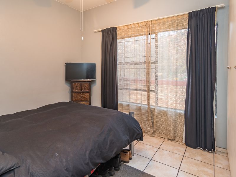 A bedroom featuring tiled flooring, a built-in cupboard, and large windows with curtain rods, providing a functional and well-lit living space.