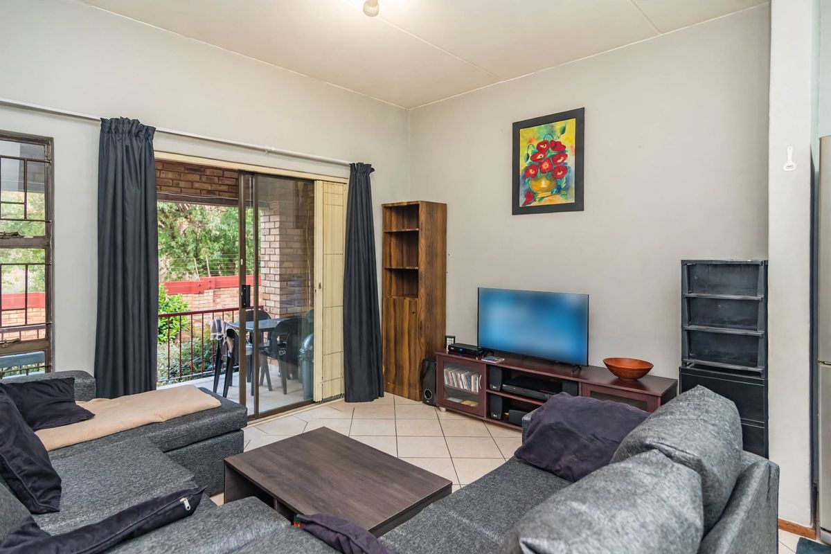 A functional living room featuring ceramic floor tiles and a sliding glass door that provides access to an outdoor balcony area.