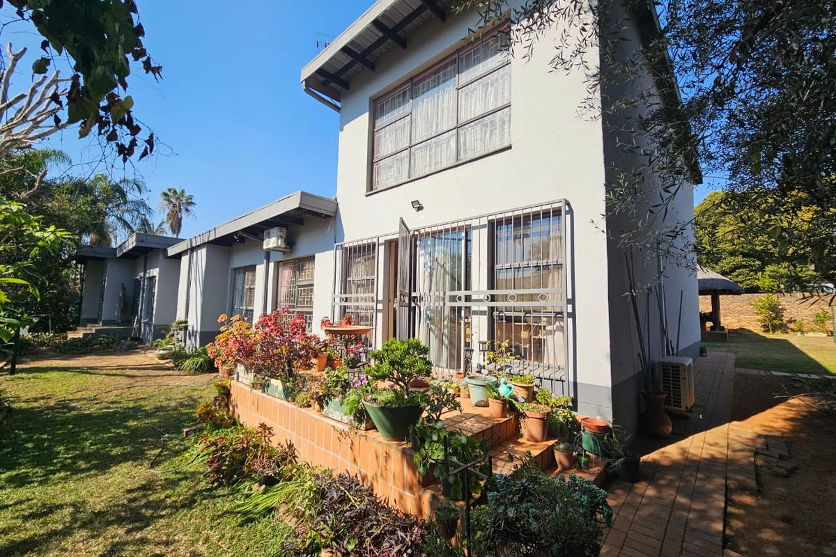 Rear view of the house featuring a terracotta tiled patio, security bars on windows, and a paved walkway leading through the garden.